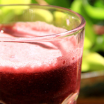 Bicchiere con succo d'uva nera illuminato dalla luce del sole con uno sfondo di fogliame