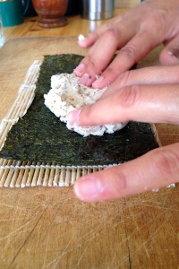Due mani stendono il composto di cavolfiore sull'alga nori