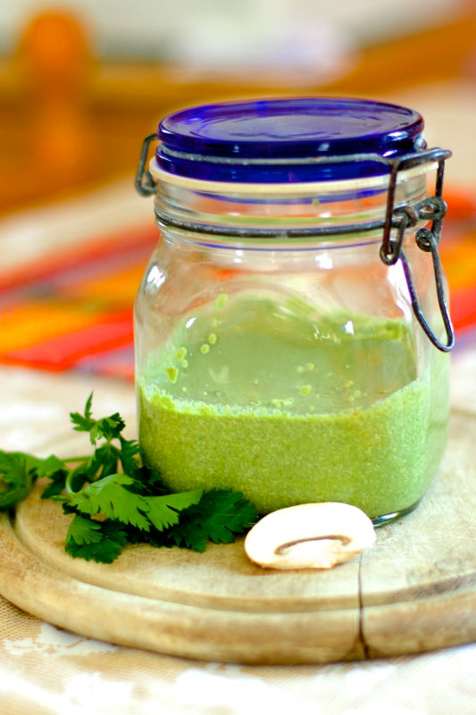 Un barattolo di salsa verde con accanto del coriandolo e funghi freschi