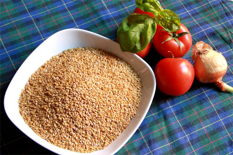 Un piatto con semi di lino. Accanto alcuni pomodori, basilico e una cipolla su tovaglia blu a righe.