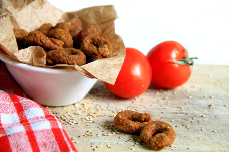 Alcuni taralli crudisti in primo piano, sullo sfondo dei pomodori rossi.