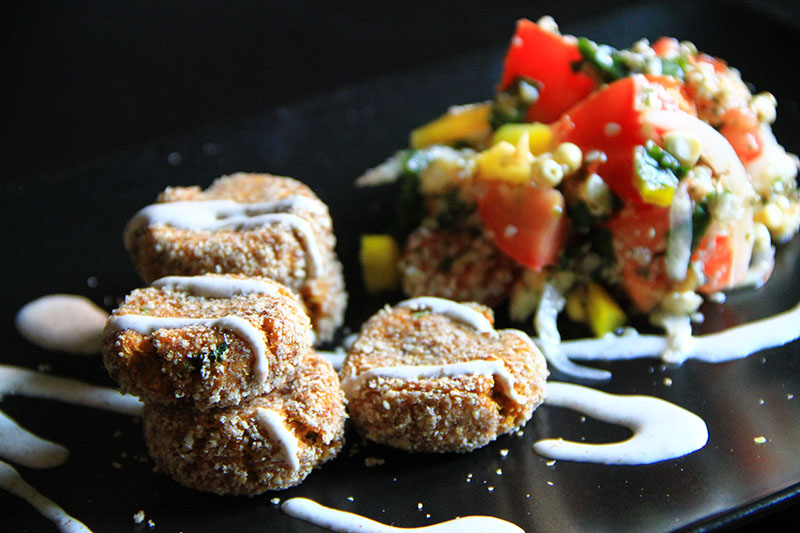 Falafel crudisti su piatto nero, accanto un tabbouleh e salsa allo yogurt