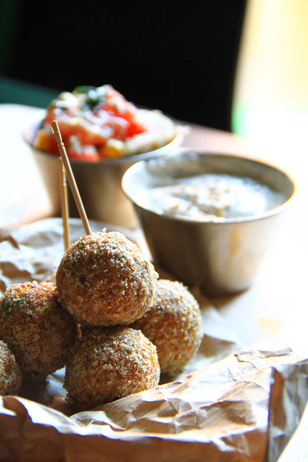 Alcuni falafel tondi uno sull'altro sopra della carta da pane, sullo sfondo una salsa bianca  e un insalatina