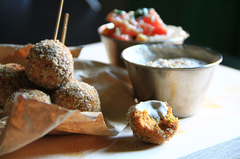 Alcuni falafel tondi uno sull'altro sopra della carta da pane, in primo piano un falafel morso con un po' di salsa bianca