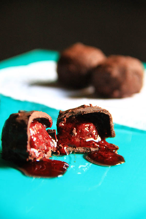 Un cioccolatino a metà in primo piano, con il succo che viene fuori. Sullo sfondo die cioccolatini interi.