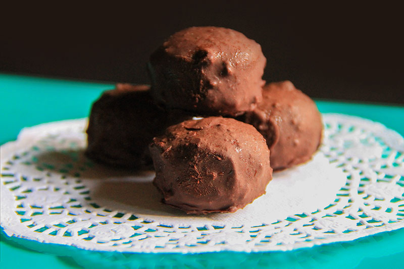 Quattro Cioccolatini crudisti ripieni di succo di more su un centrino di carta bianco.