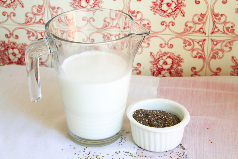 Una brocca di vetro piena di latte e una ciotola di ceramica bianca piena di semi di chia